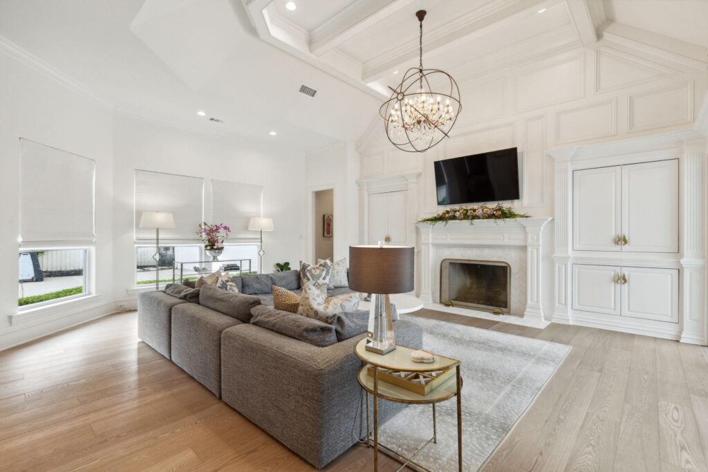 Living room with vaulted ceiling, gray sectional sofa, white fireplace with built-in cabinetry, and hardwood floors